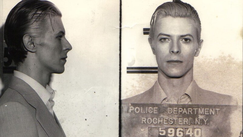 Black and white mugshot showing profile and front views of a man with a police department identification placard.