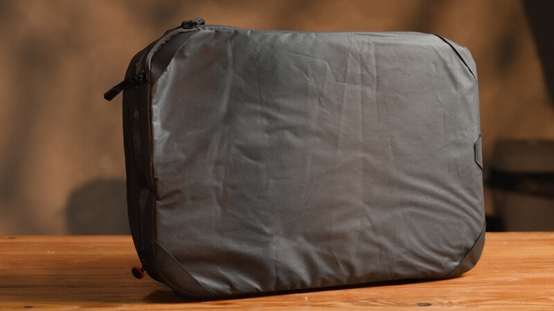 Gray padded laptop case with black trim and zipper, positioned on wooden surface against blurred background.