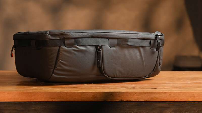 Black padded waist bag with multiple compartments displayed on a wooden surface.