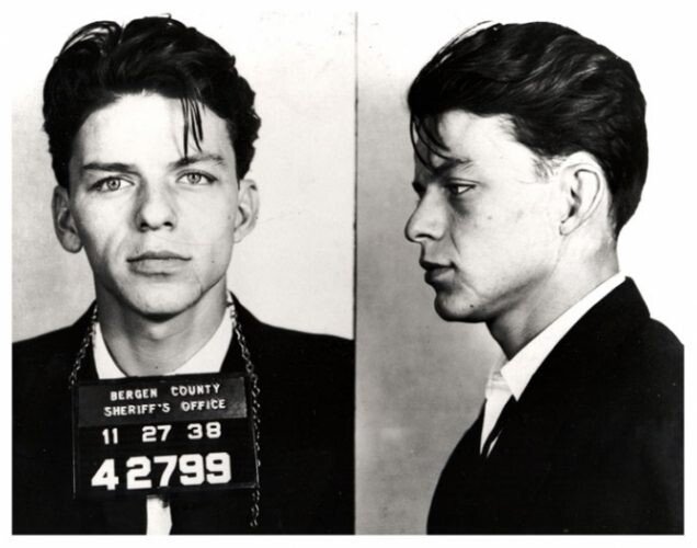 Black and white mugshot showing front and side profile views of a man with dark hair wearing a dark suit.