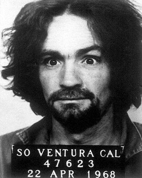 Black and white mugshot portrait of a man with long dark hair and beard, with identification text and date visible.