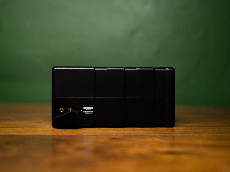Black portable battery pack or power bank with indicator lights on wooden surface against green backdrop.