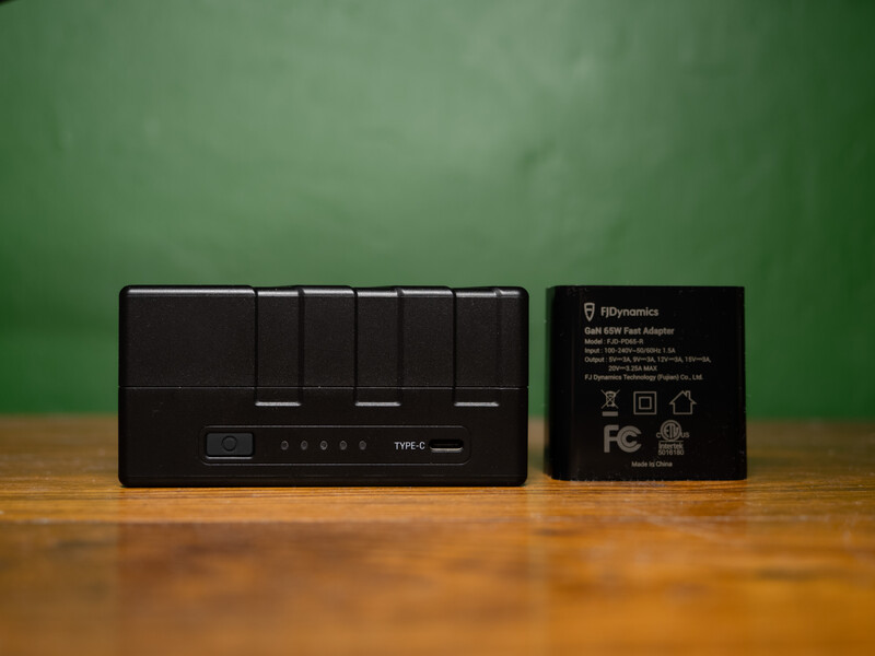 Black USB power adapter with six charging ports and a control panel displayed next to its packaging against a green background.