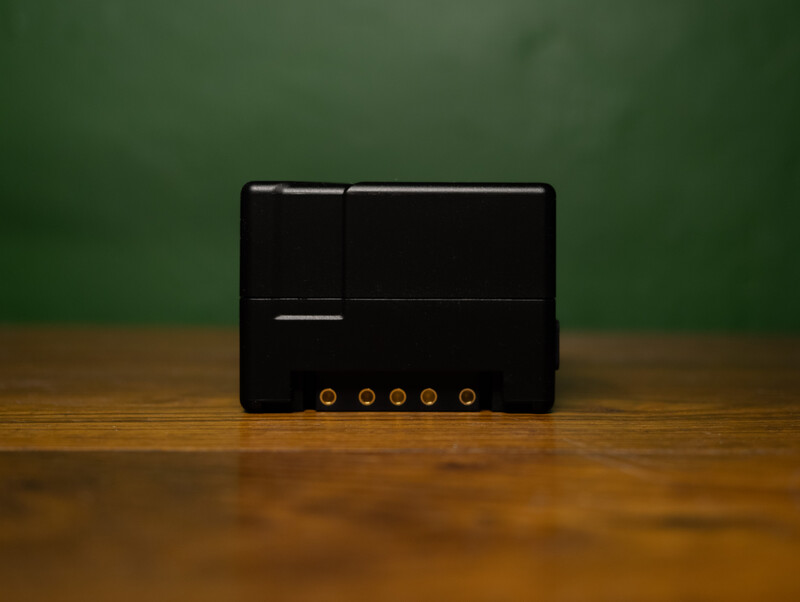 Black electronic device with five illuminated circular buttons displayed on a wooden surface against a green background.