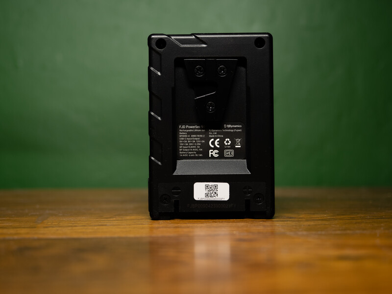 Rear view of a black speaker or audio device mounted on a wooden surface against a green wall.