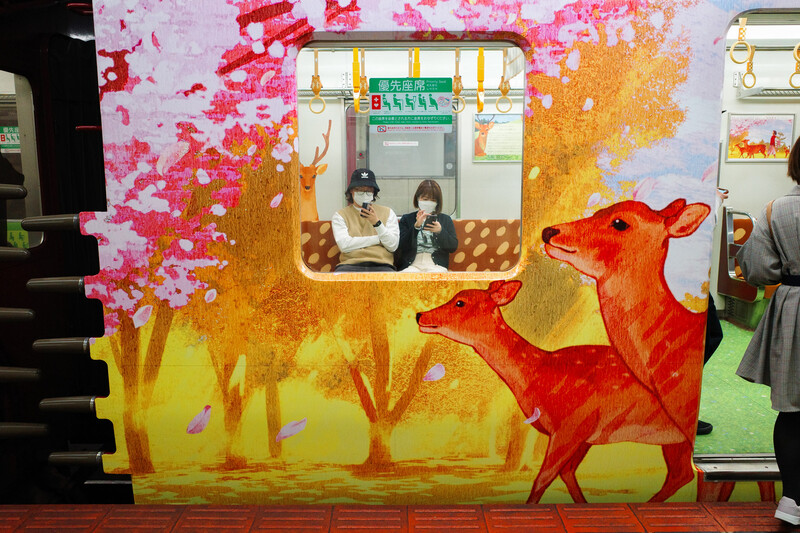 Illustration of a red deer beside a stylized yellow and pink autumn landscape with a train car window.