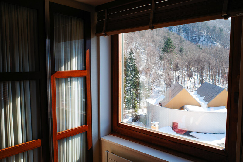 Interior view through large window frame showing snowy mountain landscape with forest and geometric white structures.