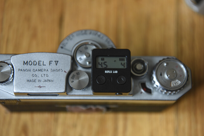 Top-down view of a vintage Panon camera with an attached light meter on a wooden surface.