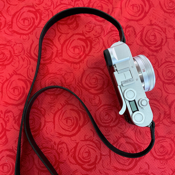 Vintage rangefinder camera with black neck strap on red rose-patterned background.