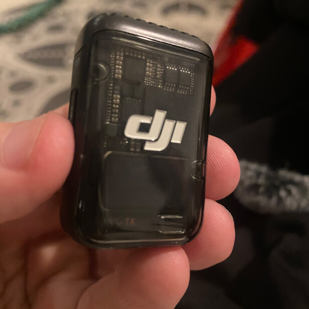 DJI Mic receiver held in hand, showing front panel with DJI branding and circuit board visible through translucent casing.