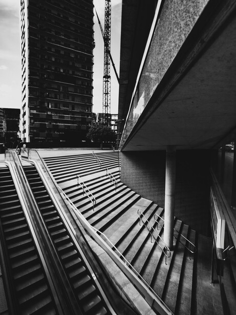 Dramatic black and white architectural photograph of converging building facades and stairs creating strong geometric lines.