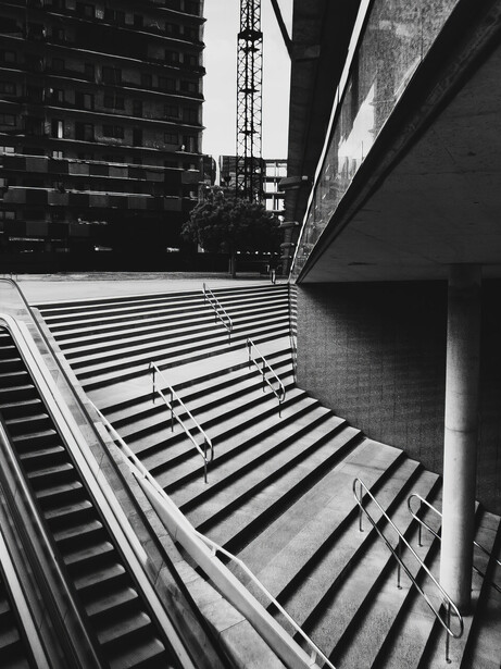 Black and white architectural photograph showing dramatic diagonal stairs and building lines converging upward.
