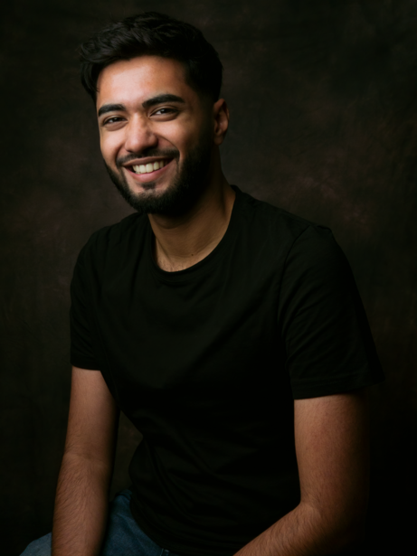 Man wearing black t-shirt smiling at camera against dark background.