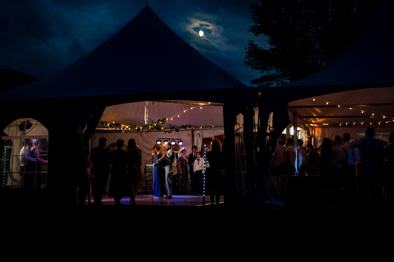 Illuminated event tent at night with guests inside and moonlit sky above.