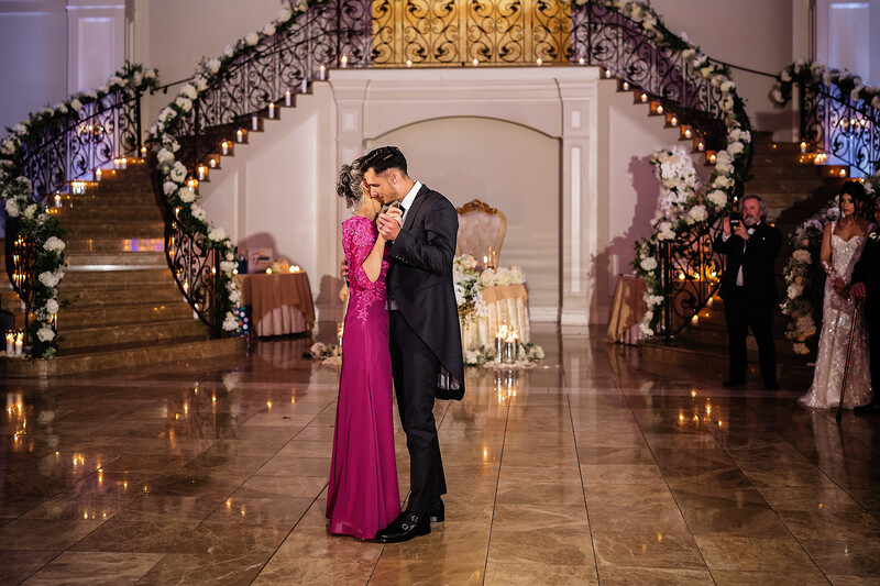 Couple in formal attire dancing under a decorated archway in an elegant ballroom.