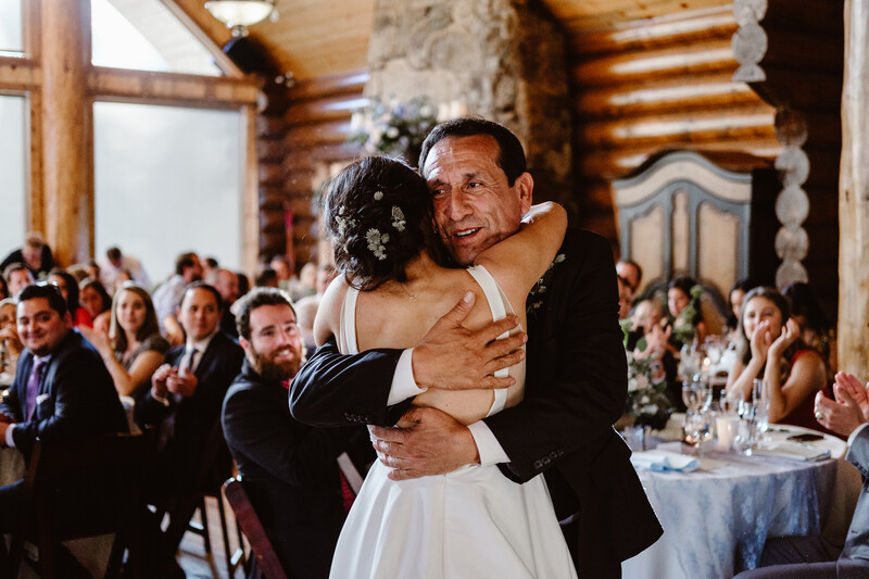 Groom embracing bride during first dance at rustic log cabin wedding reception.
