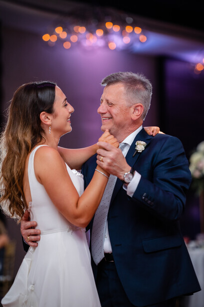 Bride and groom share their first dance at an indoor wedding reception with warm bokeh lighting overhead.