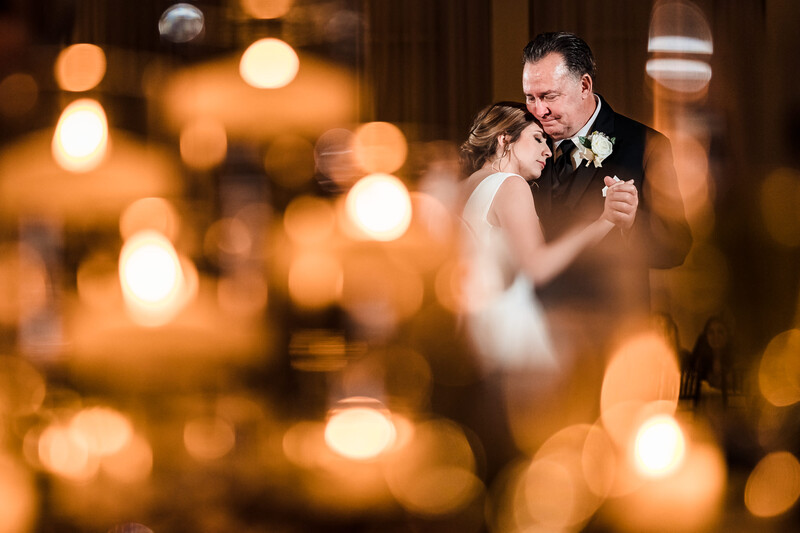 Couple dancing during first dance with warm bokeh lights in background.