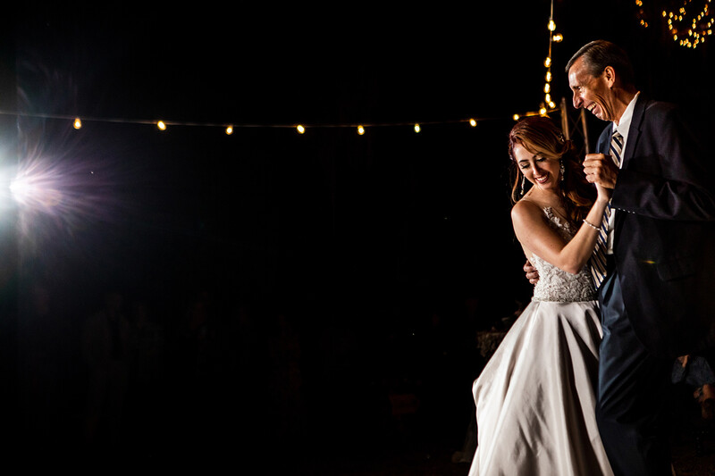 Bride and groom dancing under string lights at night.