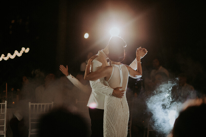 Couple dancing at night wedding reception with dramatic backlighting and atmospheric fog effects.