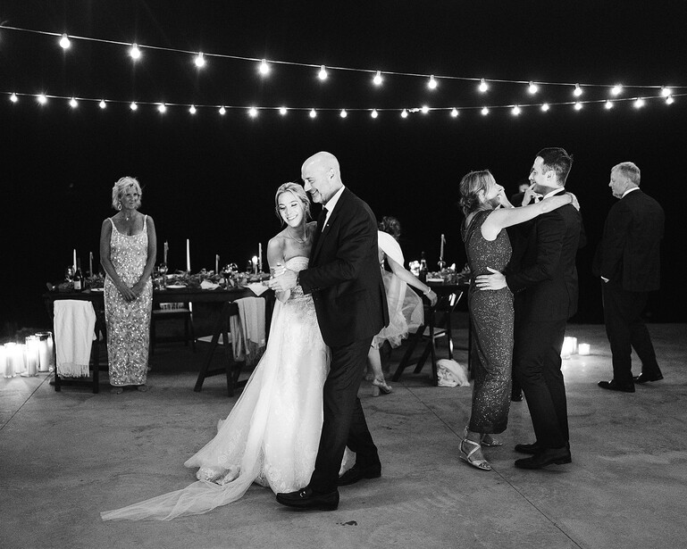 Bride and groom dancing at outdoor evening wedding reception under string lights.