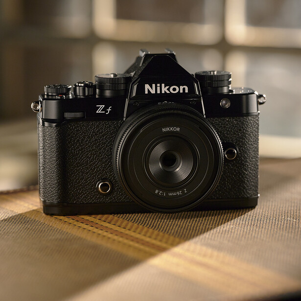 Nikon Z f mirrorless camera with prime lens on wooden surface with warm window light.