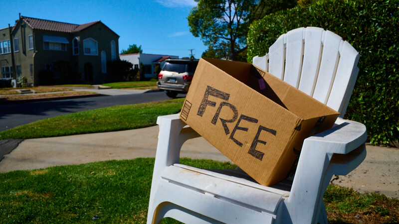 White Adirondack chair on a suburban curb with a cardboard box labeled "FREE" placed in the seat.
