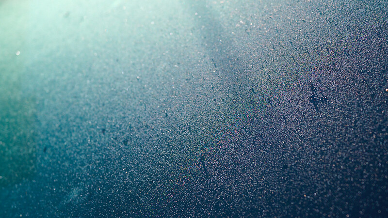 Abstract gradient background with particles and light rays transitioning from turquoise to deep blue.