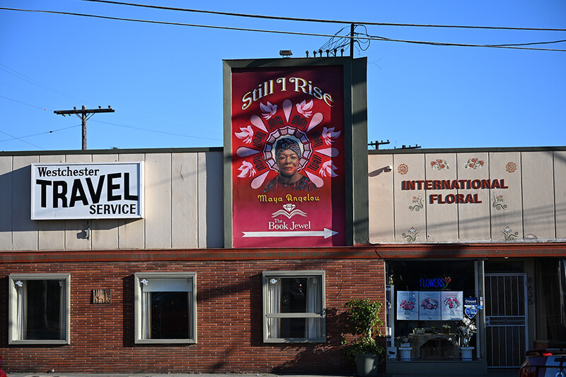 Brick storefront with large red vintage neon sign and three business banners under clear blue sky.