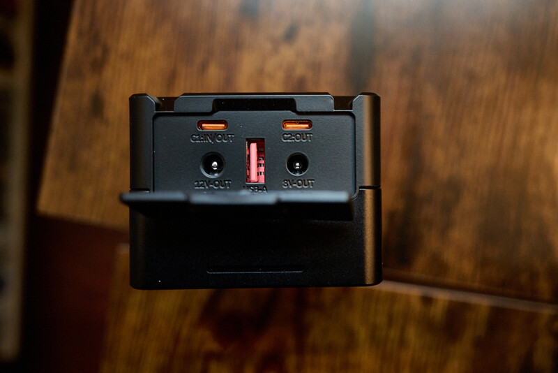 Black battery charger with dual USB ports and indicator lights mounted against a wooden surface.