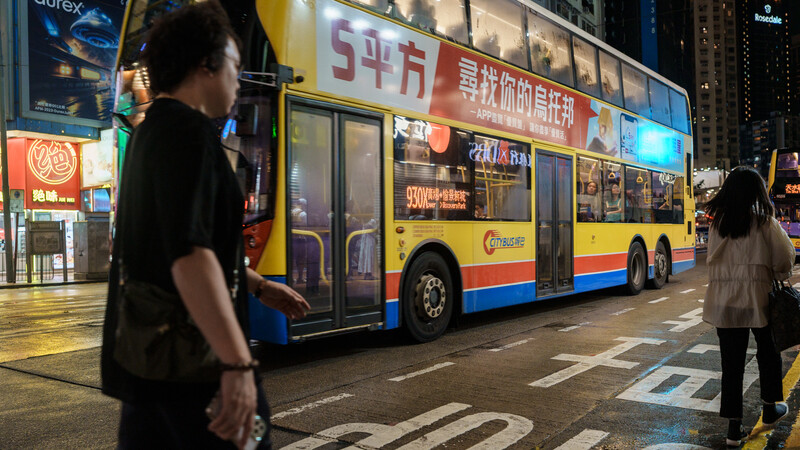 Double-decker bus with yellow, red, and blue livery stopped on wet urban street at night.