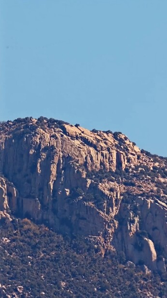 Rocky mountain ridge with columnar basalt formations against clear blue sky.