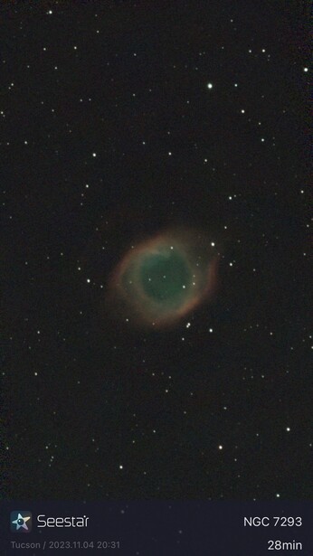 NGC 7293 planetary nebula with green central disk surrounded by reddish outer shell against starfield.