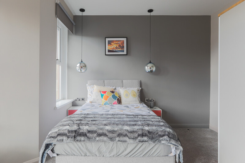 Modern bedroom with gray accent wall, pendant lighting, and colorful patterned bedding.