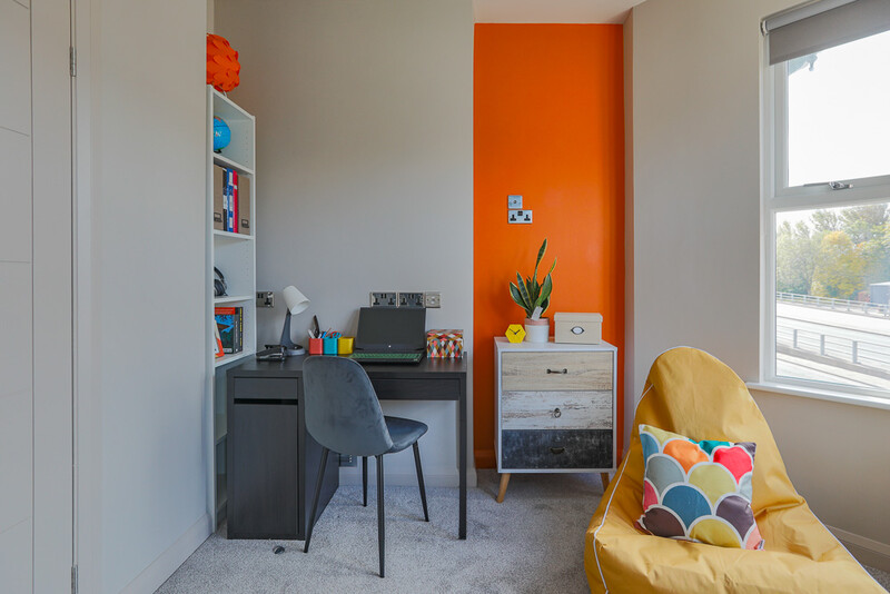 Bright home office with orange accent wall, gray desk setup, and yellow armchair by window.