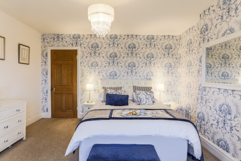 Bedroom with blue and white toile wallpaper, centered bed with blue accents, and symmetrical bedside lighting.