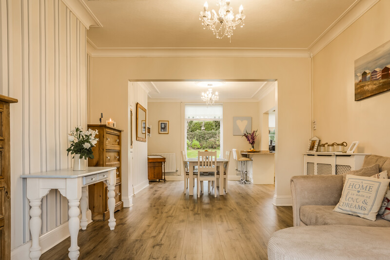 Bright, airy living room with cream walls, hardwood floors, fireplace, and multiple chandeliers.