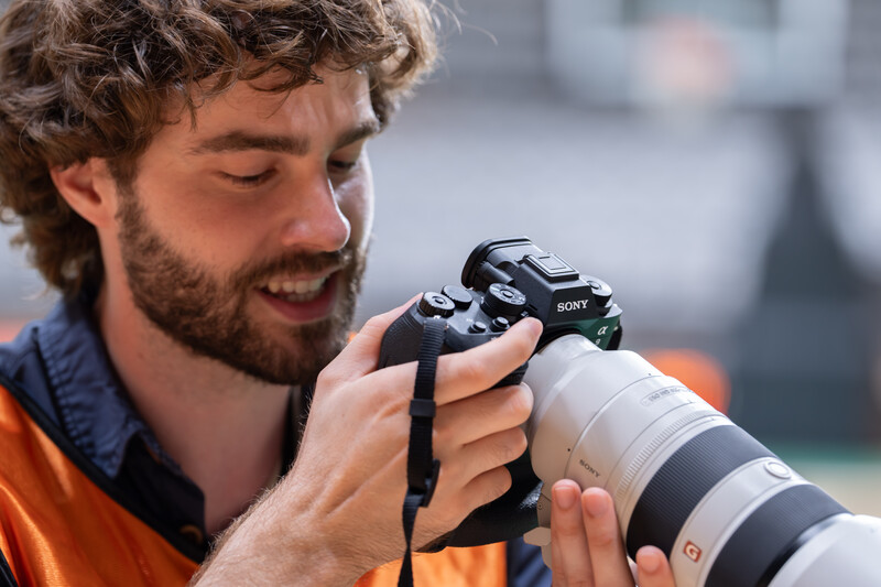 Photographer holding a Sony mirrorless camera with a telephoto lens, smiling while reviewing shots.