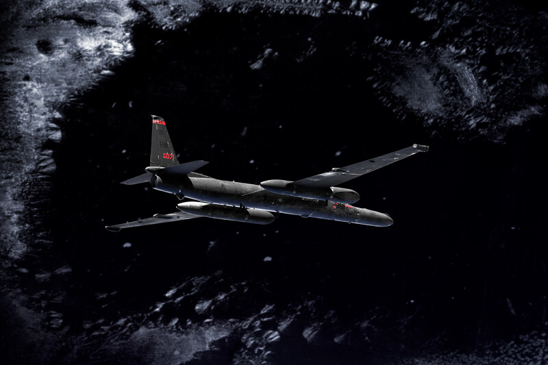 Military transport aircraft flying over snow-covered mountainous terrain at night.