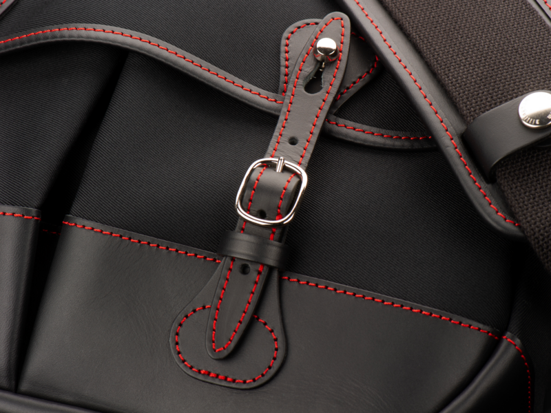 Close-up of black camera bag with red stitching and leather straps with metal buckle.