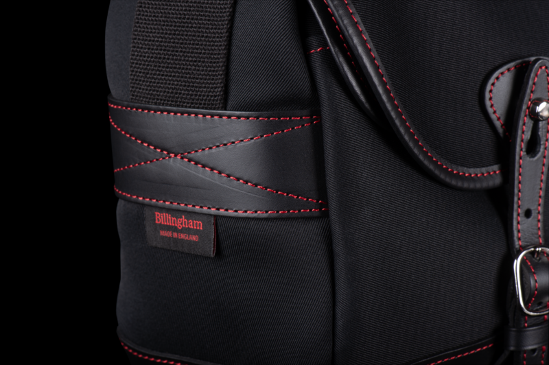 Detail of a black camera bag with red stitching and leather straps.
