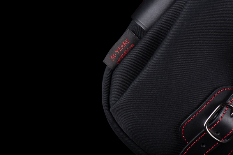 Close-up of a black camera bag or case with red stitching and text details against a dark background.