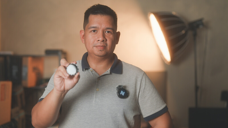 Man holding a white color checker card in a studio with professional lighting setup visible in background.