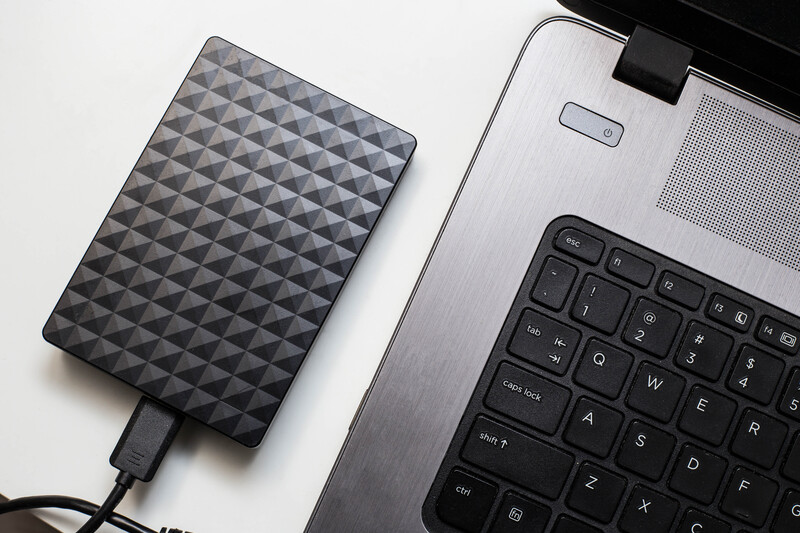 External hard drive with geometric diamond pattern beside laptop keyboard on white surface.
