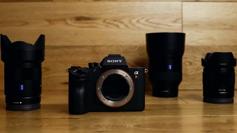 Sony a7 mirrorless camera body surrounded by four interchangeable lenses on wooden surface.
