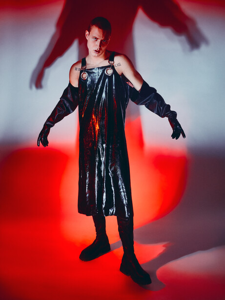 Person in black sleeveless dress posed against red and white gradient backdrop with dramatic shadow silhouette.