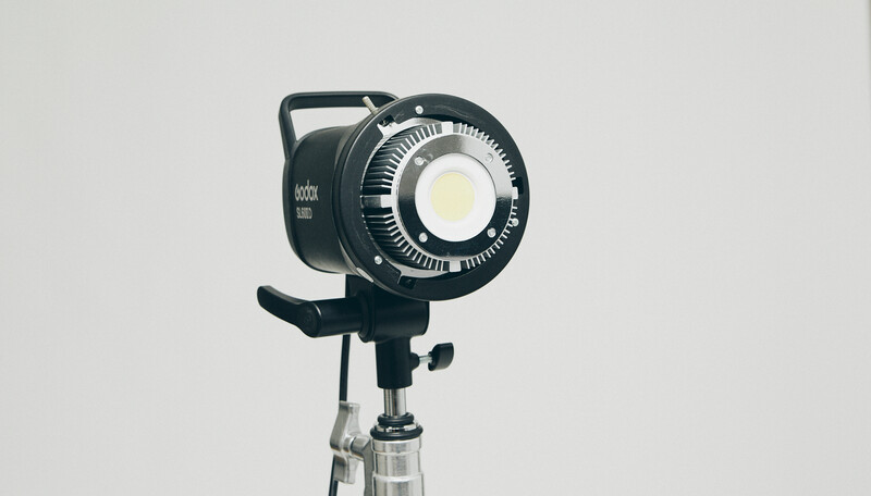 Professional LED spotlight with circular diffuser mounted on a tripod stand against neutral background.