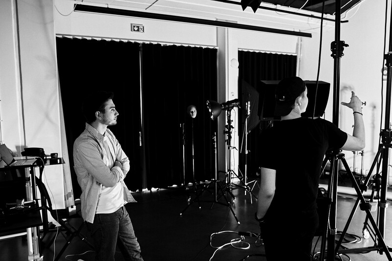 Two people in a black and white studio setting with professional lighting equipment and microphones.