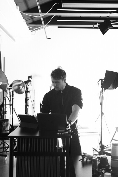 Photographer operating camera on tripod in studio with professional lighting setup overhead.