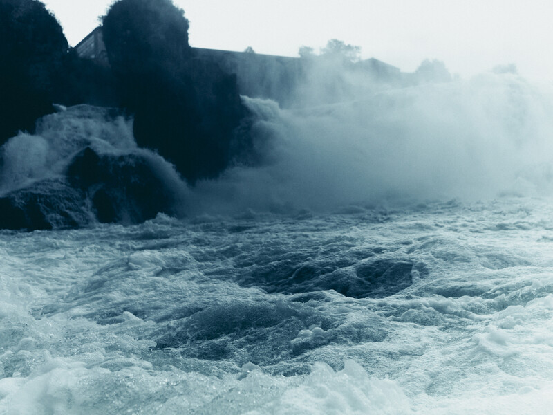 Powerful waves crash against dark rocky formations shrouded in sea spray and mist.